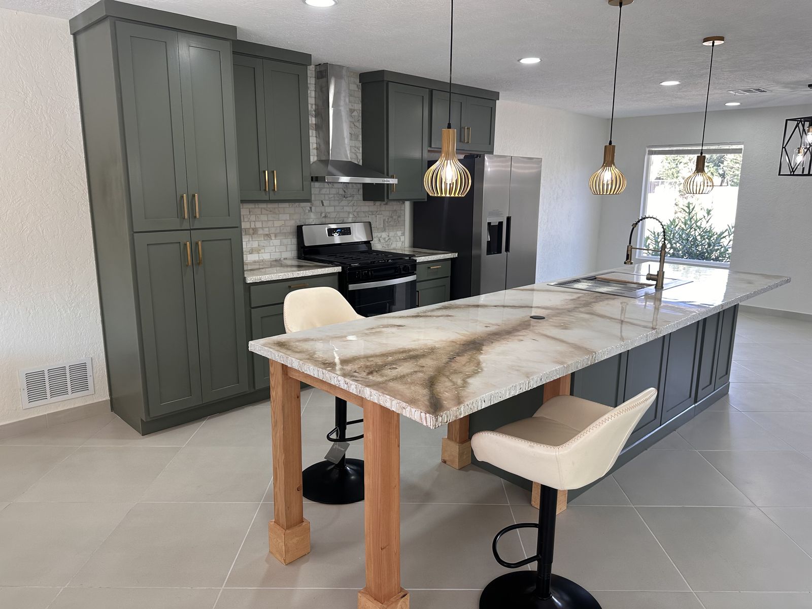 Sage green shaker kitchen with a long marble waterfall island, brass hardware and pendant lights
