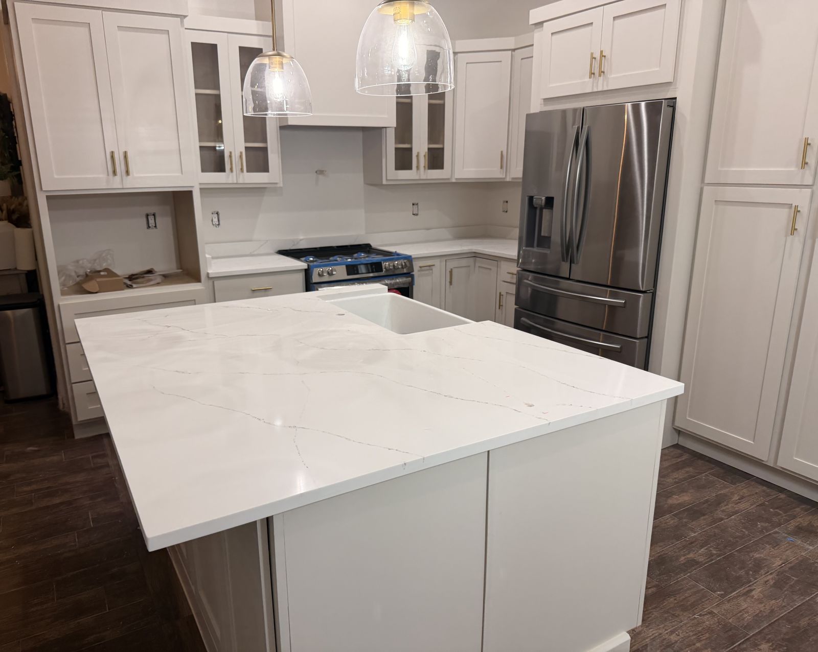 White shaker kitchen island with marble-look top, gold pulls and glass pendant lights