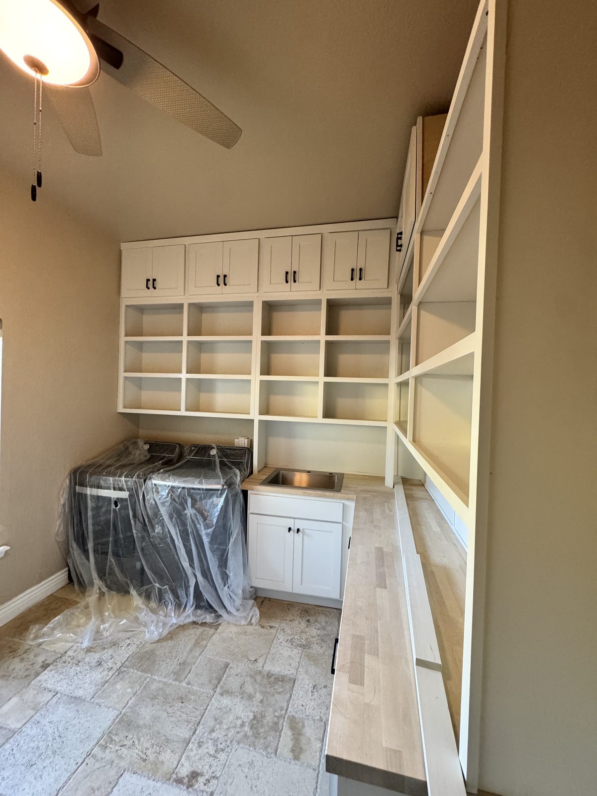 Wide view of the custom white laundry room and pantry with open shelving, butcher-block countertops and a tile floor