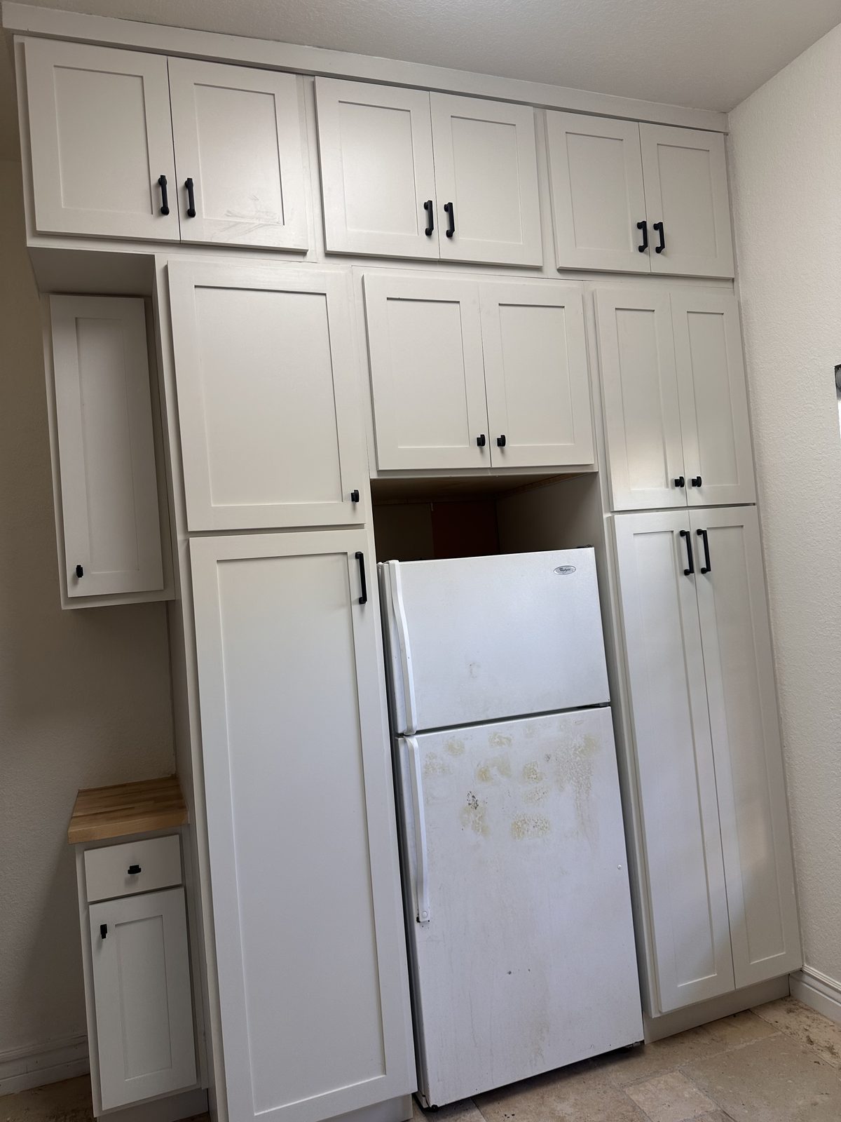 Tall white shaker pantry cabinet wall built around the refrigerator, with black pulls
